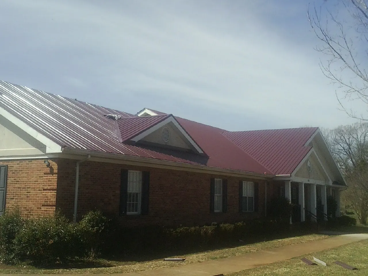 Red metal roof with gabled entries on a long brick building, from a Hail Damage Roof Repair job in Temecula