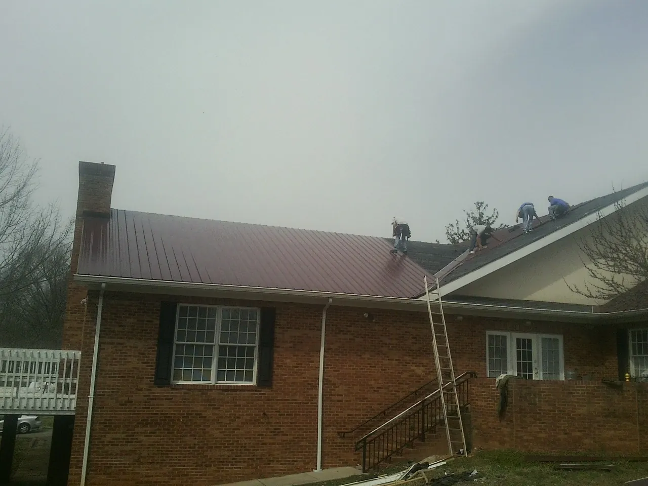 Crew setting red metal roofing panels on a brick home in Temecula