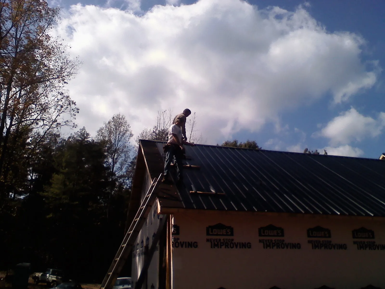 Roofer fastening dark metal panels high against a cloudy sky, from a Roof Inspection job in Temecula