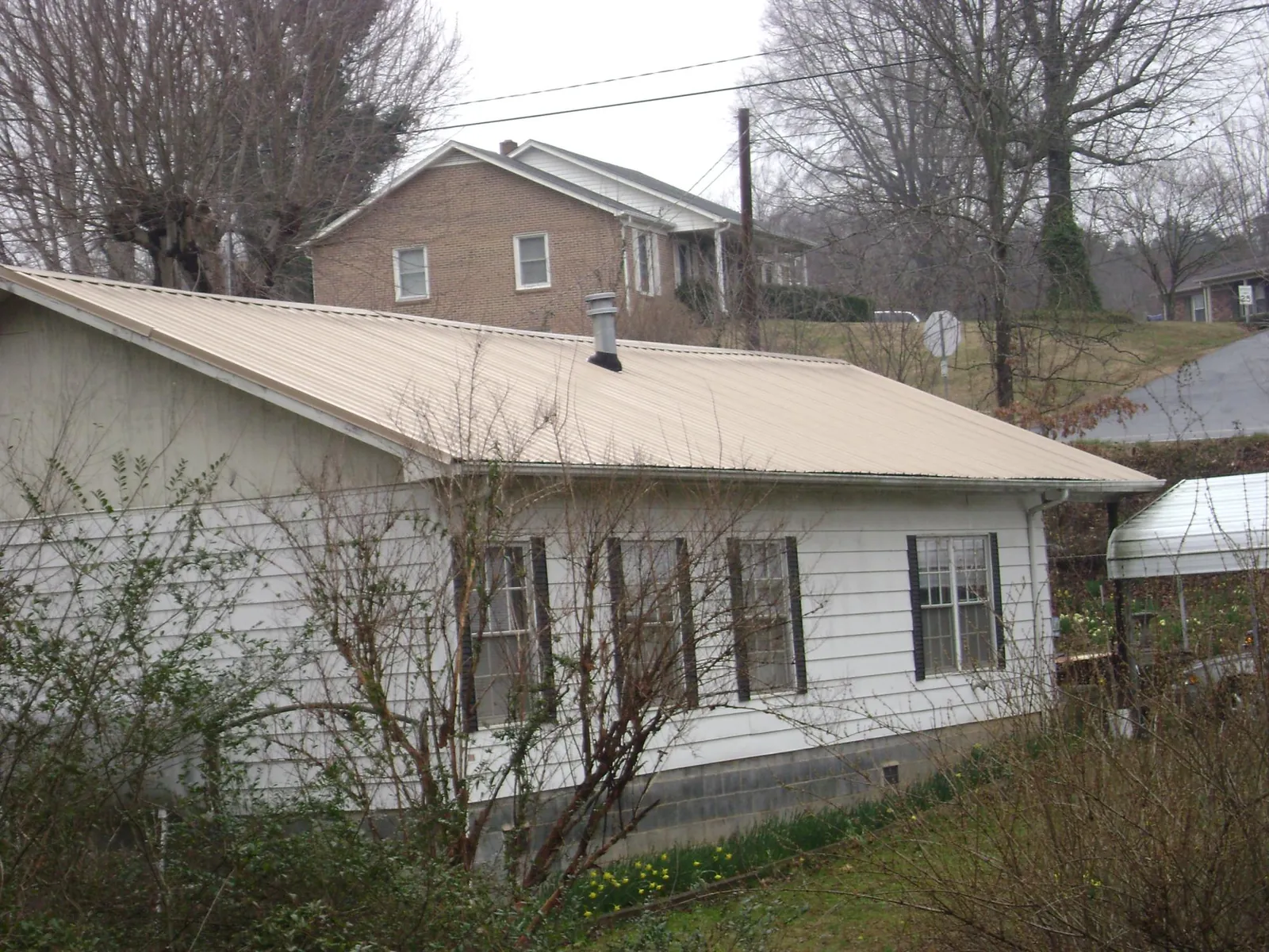 Tan metal roof on a white sided house set into a hillside — Commercial Roofing by Roofing Brothers in Temecula